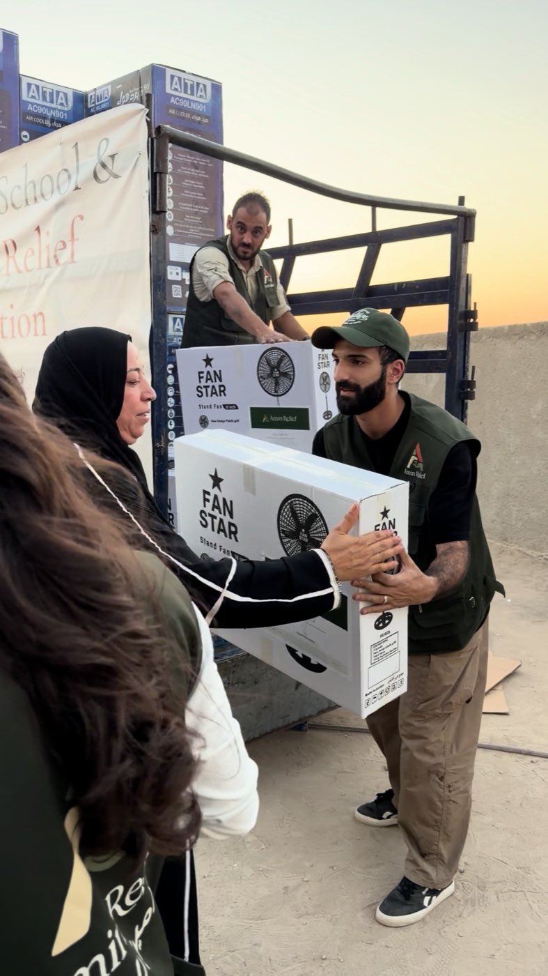 An Amin Relief volunteer handing a boxed standing fan to a woman at the distribution